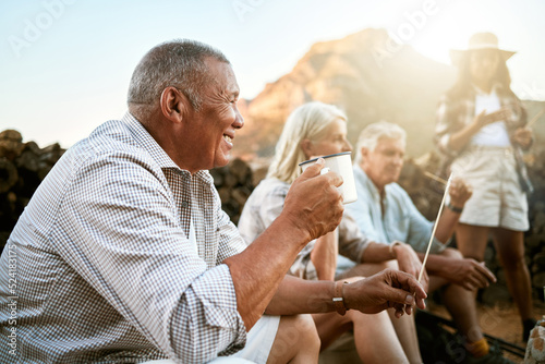 . Relaxed senior camping with friends, taking a break and drinking a cup of coffee while enjoying retirement keeping healthy outdoors in nature. Smiling retired man on a getaway wellness retreat. photo