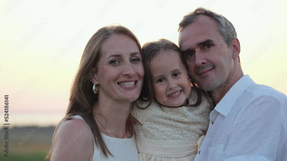 Portrait of happy family smiling at back sunlight. Parents and daughter enjoy life together walking on evening meadow with smile closeup Portrait of happy family smiling at back sunlight. Parents and daughter enjoy life together walking on evening meadow with smile closeup