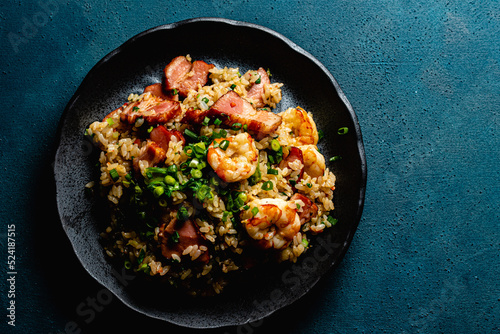 Fried rice with bacon and shrimp against a blue plaster design board. 