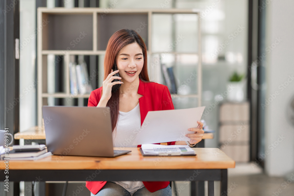 Young Business Asian woman talking on a smartphone and working in an office. Asian female Business accountant Documents data sitting at his workplace. Young Business Asian woman talking on a smartphone and working in an office. Asian female Business accountant Documents data sitting at his workplace.