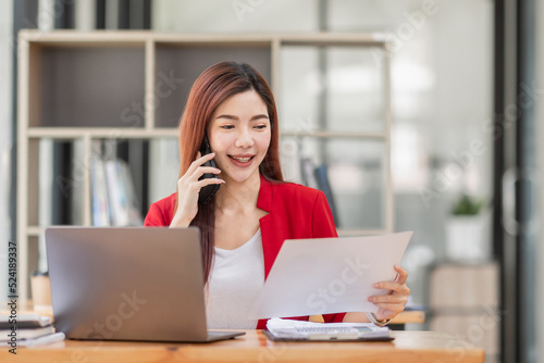 Young Business Asian woman talking on a smartphone and working in an office. Asian female Business accountant Documents data sitting at his workplace.