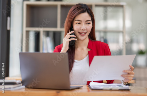 Young Business Asian woman talking on a smartphone and working in an office. Asian female Business accountant Documents data sitting at his workplace.