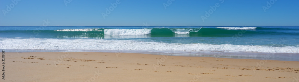 Panorama of surf waves rolling in to the beach on a calm, sunny, winter day.