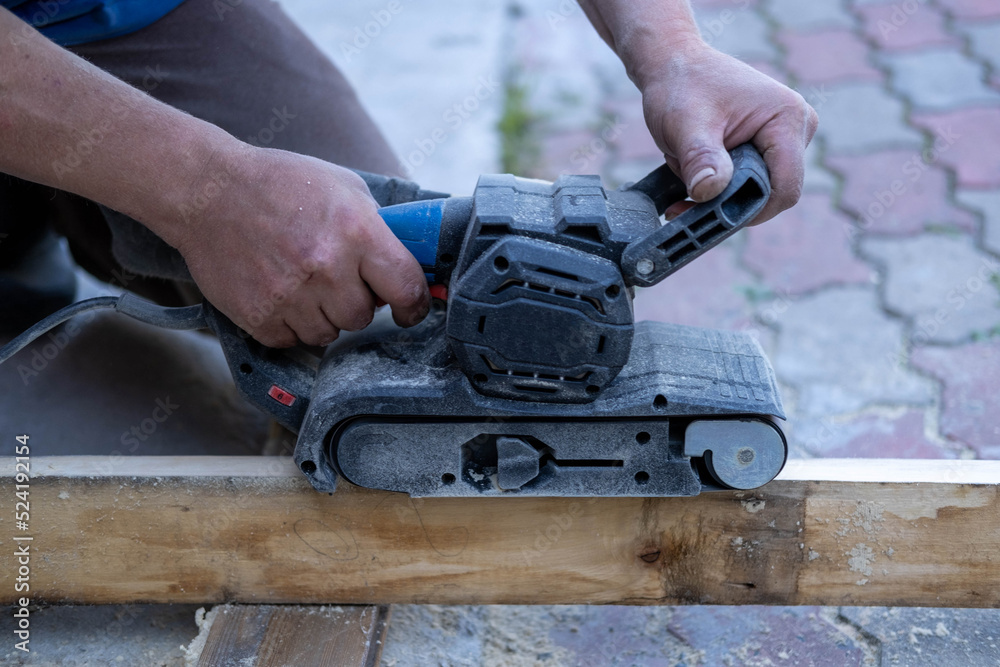 The man's hands are holding a grinding machine. Processing of a furniture part by a machine for polishing a tree. the grinding machine on a board.