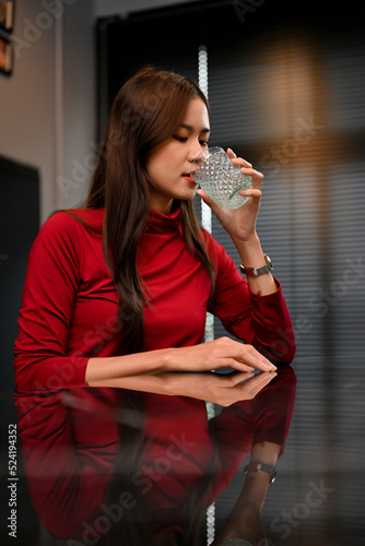 Thirsty young Asian woman enjoying refreshing drink at home. photo