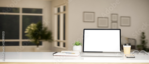 Modern working tabletop with laptop mockup and copy space over blurred living room in background. © bongkarn