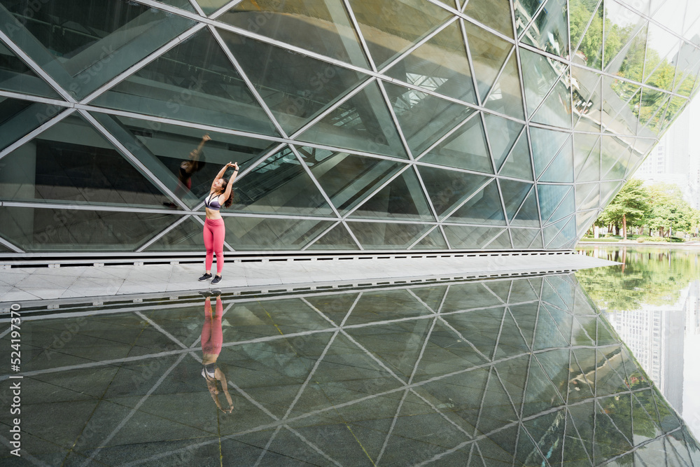Young woman stretching in front of glass building to warm up for exercise