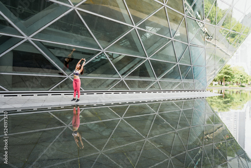 Young woman stretching in front of glass building to warm up for exercise