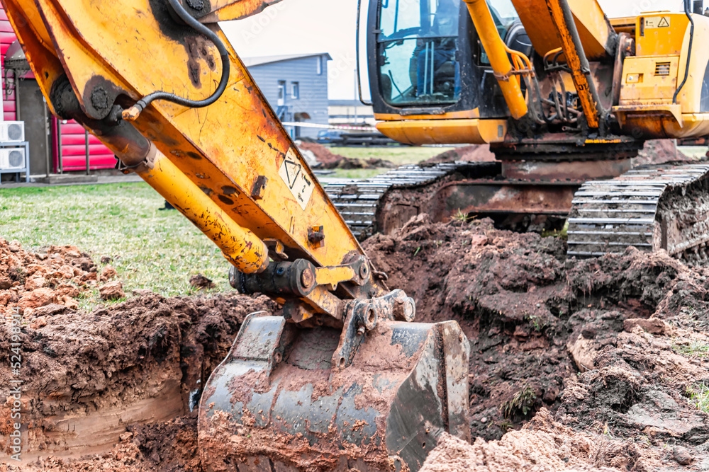 Fototapeta premium Close up of excavator bucket at construction site. The excavator is digging a trench for underground utilities. Construction equipment for earthworks.