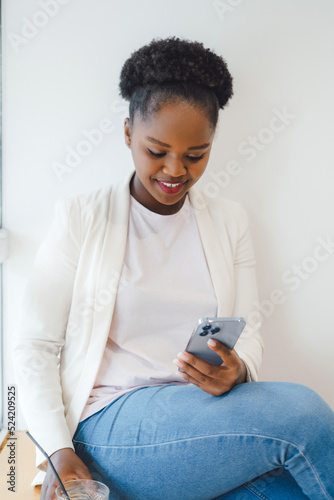 Portrait of beautiful smiling african american woman chatting on mobile phone, sitting at coffee shop during her work break. Internet technology. Internet