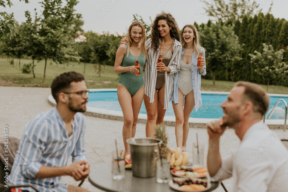 Group of young people cheering with drinks and eating fruits by the pool in the garden Group of young people cheering with drinks and eating fruits by the pool in the garden
