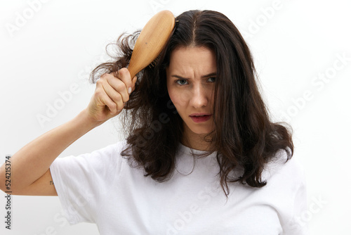 a sad, upset woman tries to comb her long, dark, tangled hair with a wooden massage comb. Hair care topics
