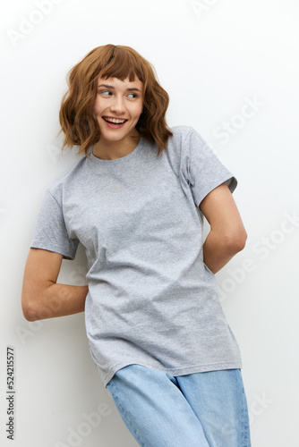 a sweet, pretty, relaxed woman is standing in stylish clothes, a T-shirt and jeans, leaning against a wall on a white background