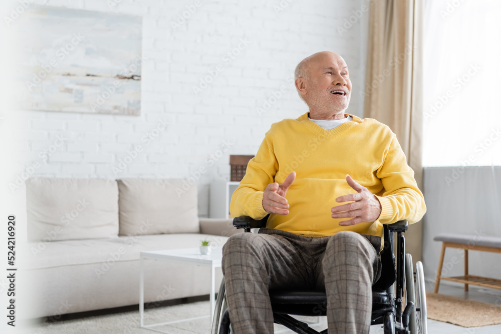 Fototapeta premium Positive elderly man looking away while sitting in wheelchair at home.