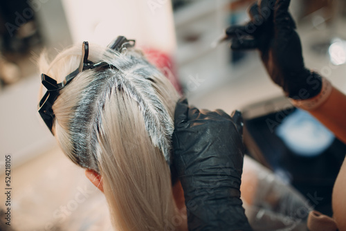 Young woman hairdresser dying hair at beauty salon. Professional hair roots coloring.