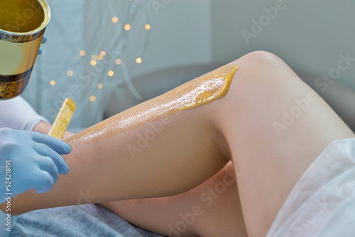 Spa Concepts. Close-up of Beautician Preparing for Wax Depilation of Woman Legs By Applying Liquid Wax With Spatula on Female Legs. photo