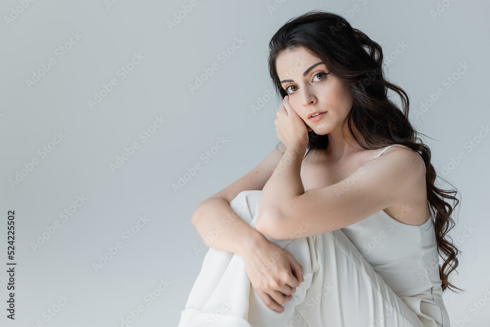 Pretty brunette woman looing at camera while sitting isolated on grey. Pretty brunette woman looing at camera while sitting isolated on grey.