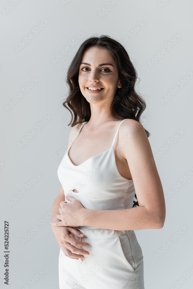 Portrait of smiling brunette woman in white clothes looking at camera isolated on grey. Portrait of smiling brunette woman in white clothes looking at camera isolated on grey.