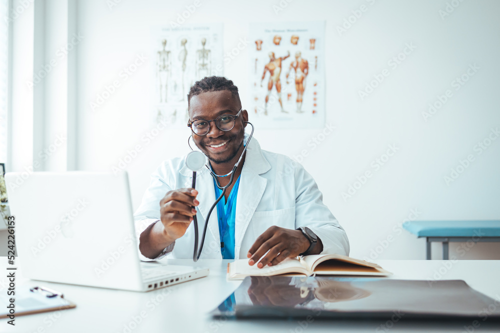 Fototapeta premium Doctor in office working on laptop. Male doctor working at office desk and smiling at camera, office interior on background. 