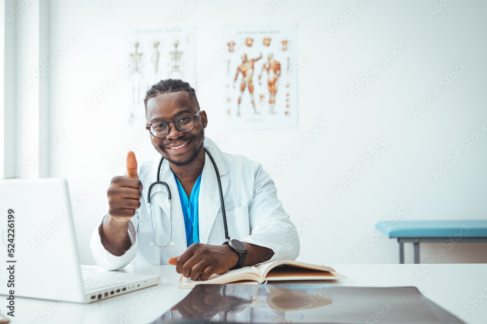 Fototapeta premium Young handsome doctor man wearing white profressional coat in office doing happy thumbs up gesture with hand. Approving expression looking at the camera showing success.