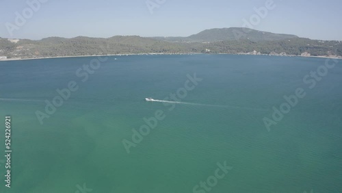 Aerial view of following a boat in front of the Troia Peninsula, in Setubal, Portugal - panoramic, drone shot photo