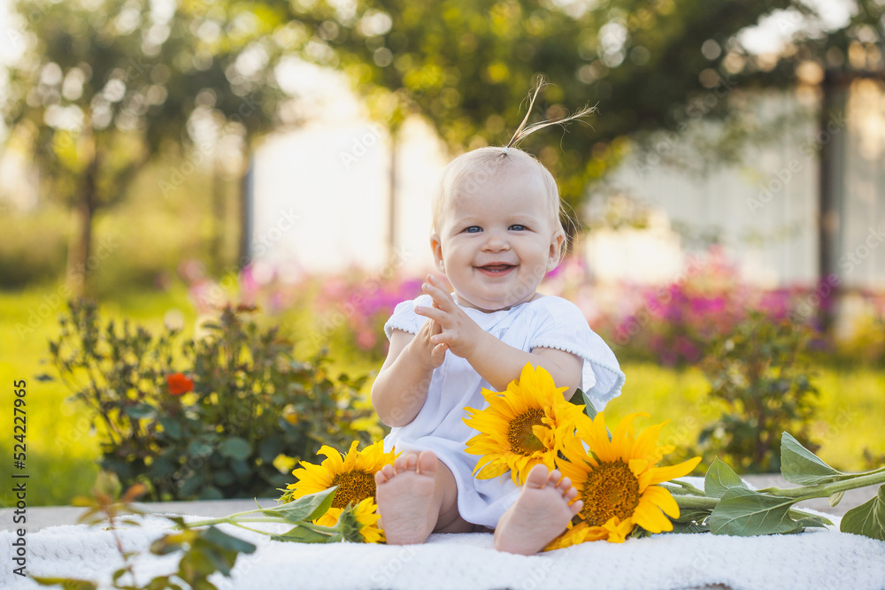 one year old baby girl in a blooming garden with a bouquet of sunflowers