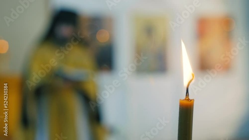 One candle burns in an Orthodox church. In the background, a monk is preaching a sermon. The priest reads a prayer standing in the church. An Orthodox priest conducts a prayer ceremony.