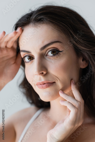 Portrait of brunette woman touching face isolated on grey.