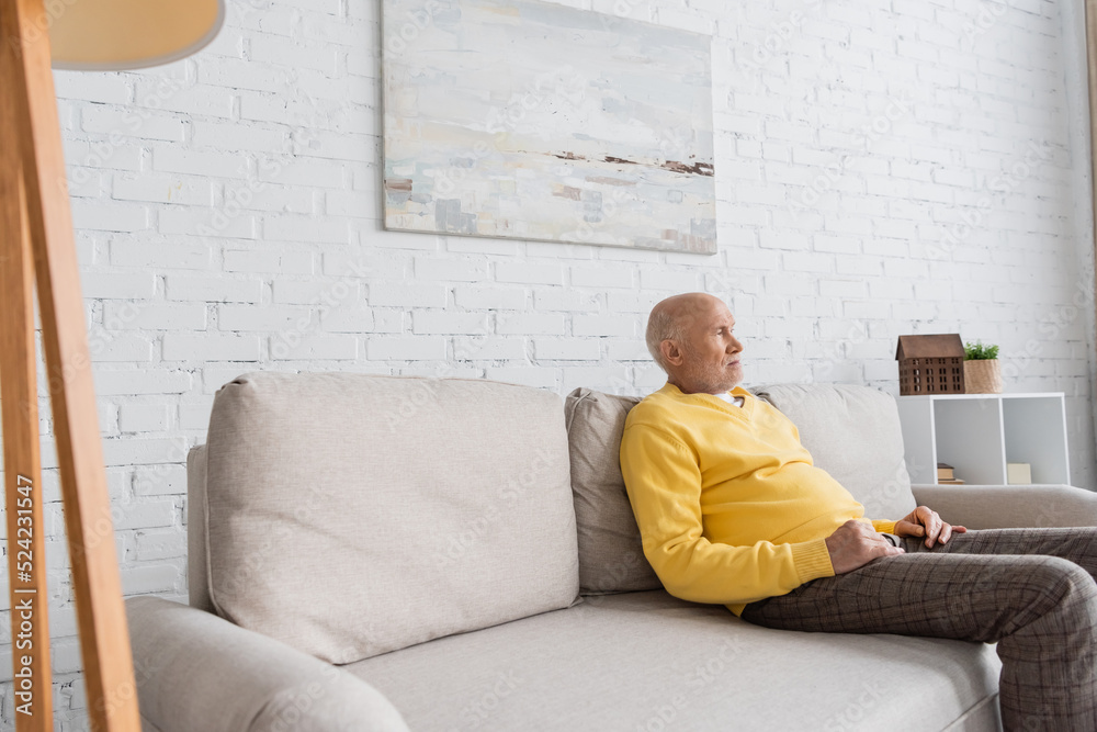 Displeased senior man looking away while sitting on couch at home. Displeased senior man looking away while sitting on couch at home.