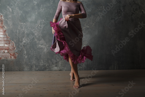 Young adult spanish woman dancing flamenco on gray vintage studio background legs close up