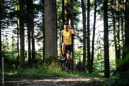 Junger dunkelhäutiger Mann in Sportkleidung spring während dem Laufen im Wald beim Trailrunning