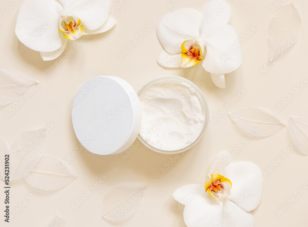Opened Cream jar with a blank lid near orchid flowers on light beige top view. Cosmetic Mockup