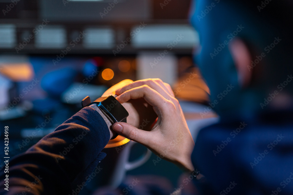 cybercrime, hacking and technology concept - close up of male hacker in dark room with smart watch and computer carries out cyber attack in dark room cybercrime, hacking and technology concept - close up of male hacker in dark room with smart watch and computer carries out cyber attack in dark room