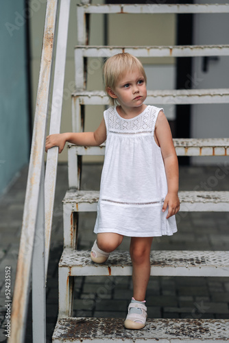 Cute little girl 4 years old wearing white dress on stairs