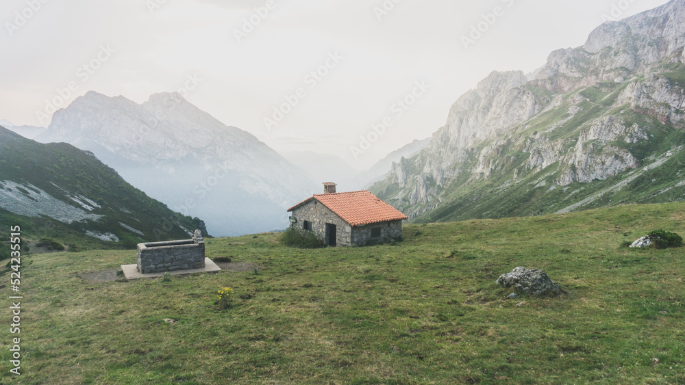 Mountain scenary with a hut in the middle and a stone fountain on its side