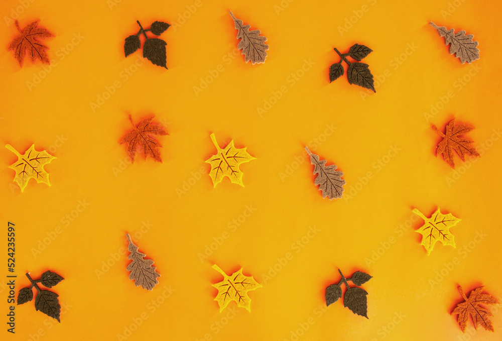 Beautiful autumn flat lay pattern of felt decoration leaves of oak and maple of yellow red orange green and brown colors on orange background. Holidays concept with copy space Beautiful autumn flat lay pattern of felt decoration leaves of oak and maple of yellow red orange green and brown colors on orange background. Holidays concept with copy space