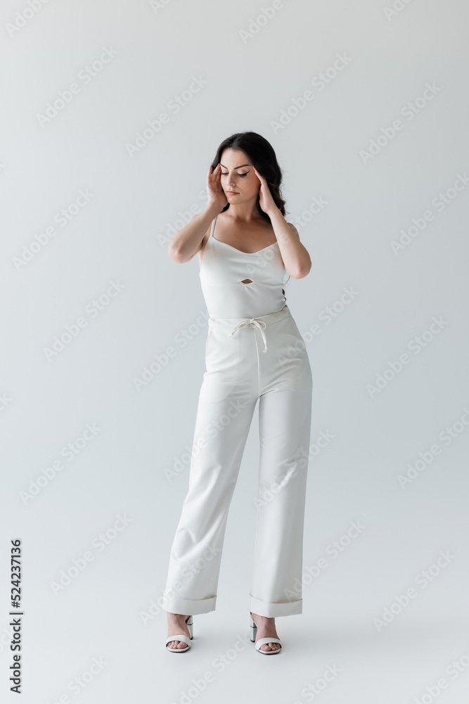 Full length of brunette model in white clothes standing on grey background. Full length of brunette model in white clothes standing on grey background.