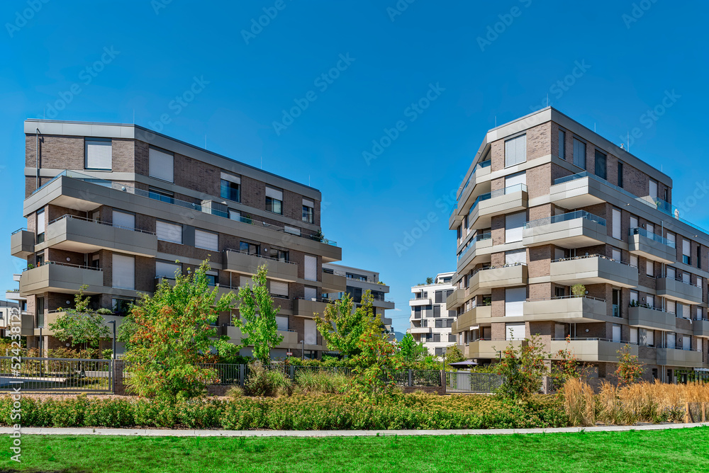 Moderne, gerade fertiggestellte Wohnhäuser mit Etagenwohnungen in einem Neubaugebiet bei sonnigem Wetter und blauem Himmel
