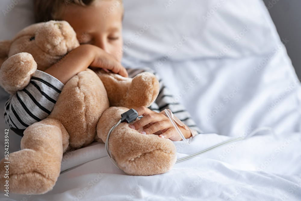 Little boy sleeping in hospital bed with teddy bear