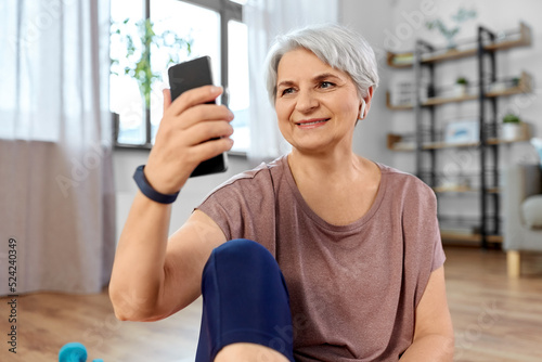 sport, fitness and healthy lifestyle concept - smiling senior woman with smartphone and wireless earphones exercising on mat at home