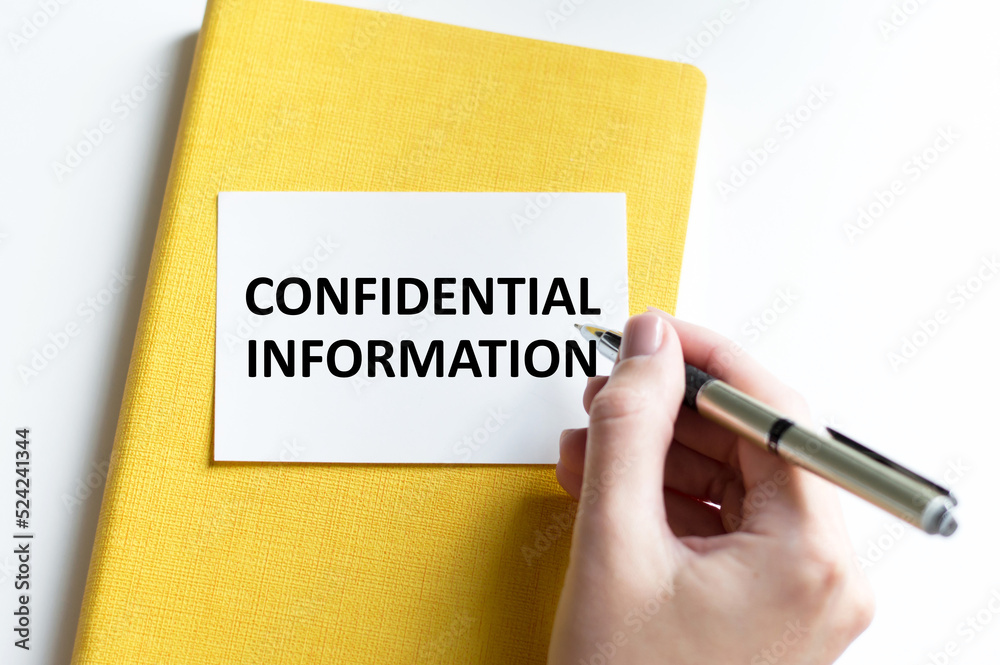 confidential information text on the card writes a person's hand next to a yellow notebook on a light background confidential information text on the card writes a person's hand next to a yellow notebook on a light background