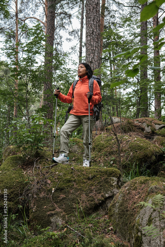 Vertical long shot of adventurous young adult Hispanic woman hiking in local mountains using trekking poles Vertical long shot of adventurous young adult Hispanic woman hiking in local mountains using trekking poles