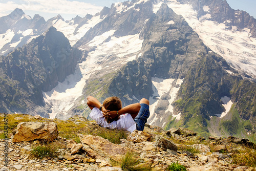 a long-haired young man, a tourist in a white T-shirt, is lying on a mountain slope