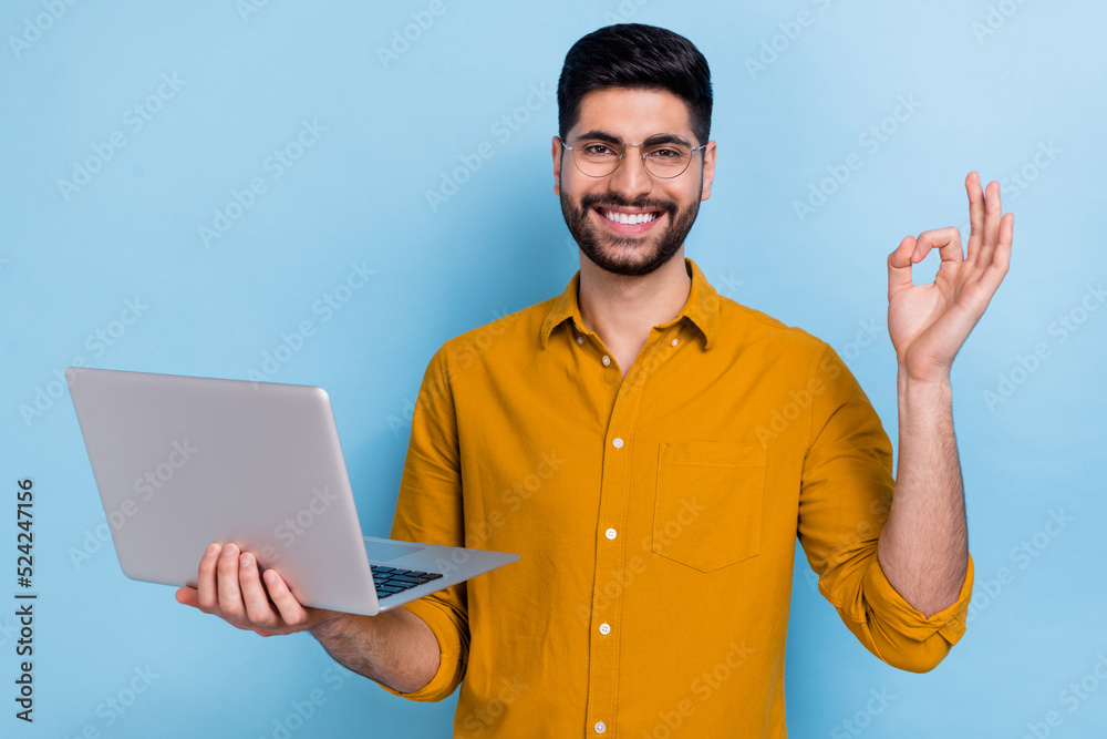 Photo of boss brunet millennial guy hold laptop show okey wear brown shirt spectacles isolated on blue color background Photo of boss brunet millennial guy hold laptop show okey wear brown shirt spectacles isolated on blue color background