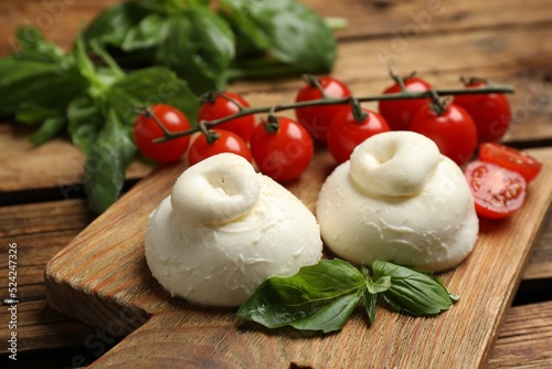 Delicious burrata cheese with basil and cherry tomatoes on wooden table, closeup