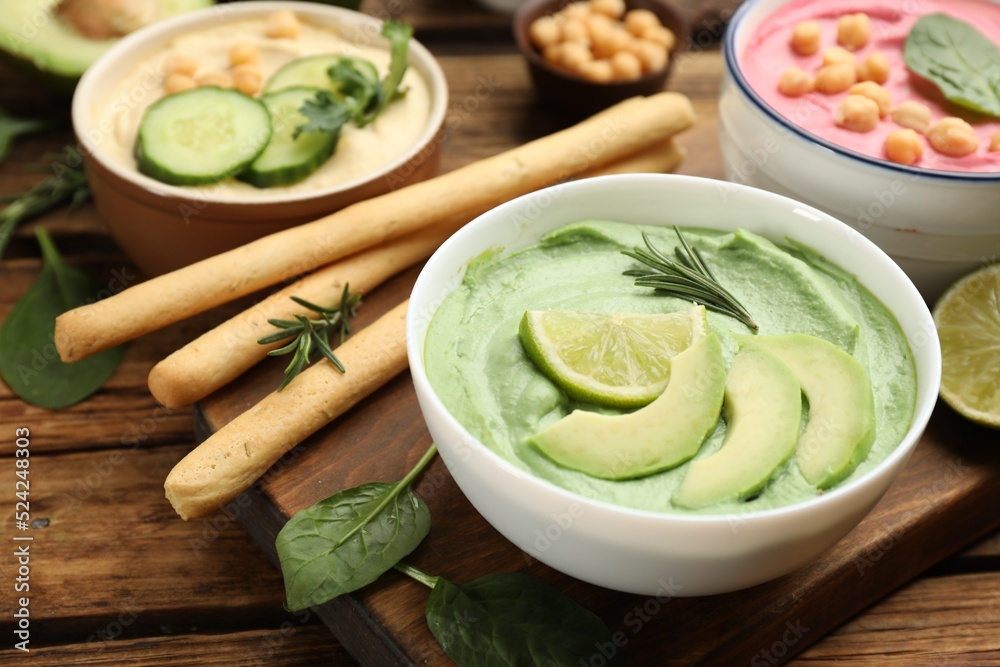 Bowl of delicious green hummus with rosemary, avocado and lime on wooden table Bowl of delicious green hummus with rosemary, avocado and lime on wooden table
