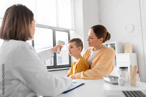 medicine, healthcare and pediatry concept - mother with sick little son and doctor measuring temperature with infrared forehead thermometer at clinic