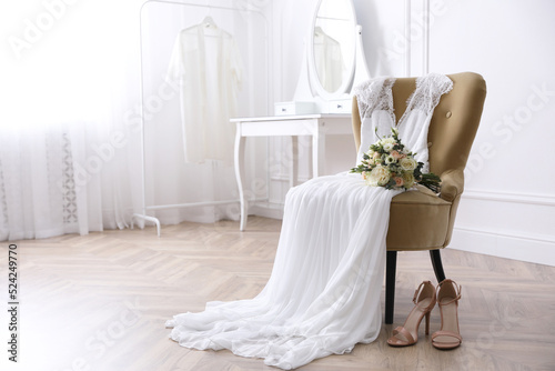 Elegant wedding dress, shoes and bouquet in room