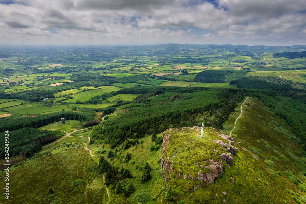 Tall white Catholic cross on top of Devils bit mountain in county Tipperary, Ireland. Aerial view. Beautiful landscape with green fields and forests in the background. Irish landscape. Tall white Catholic cross on top of Devils bit mountain in county Tipperary, Ireland. Aerial view. Beautiful landscape with green fields and forests in the background. Irish landscape.