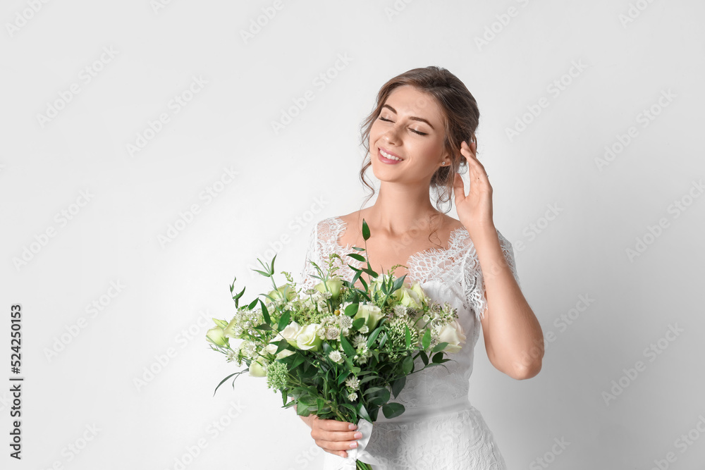 Young bride wearing wedding dress with beautiful bouquet on light background Young bride wearing wedding dress with beautiful bouquet on light background
